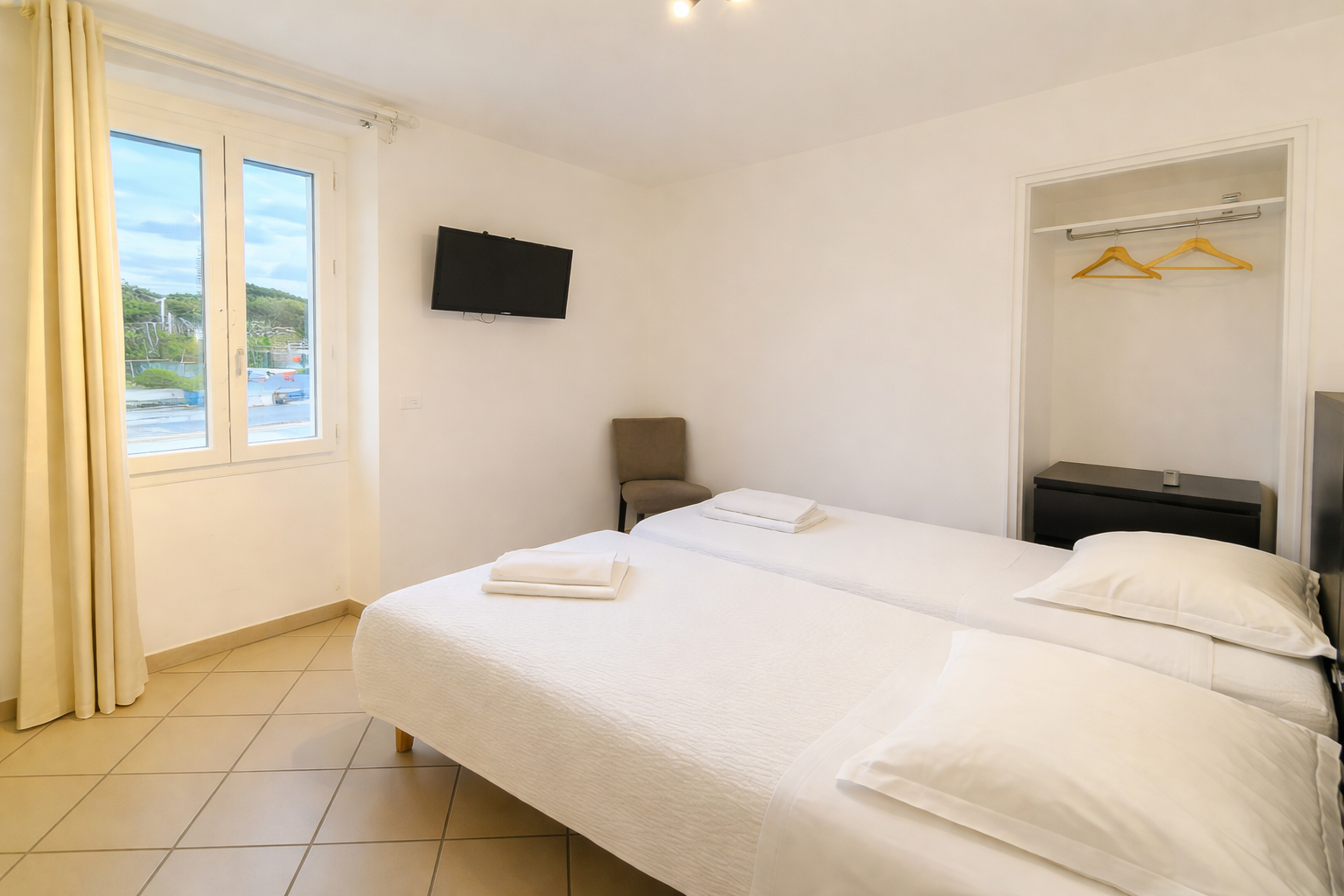 Chambre twin à La Croix Valmer avec deux lits simples, télévision murale et fenêtre lumineuse à l’hôtel La Cigale